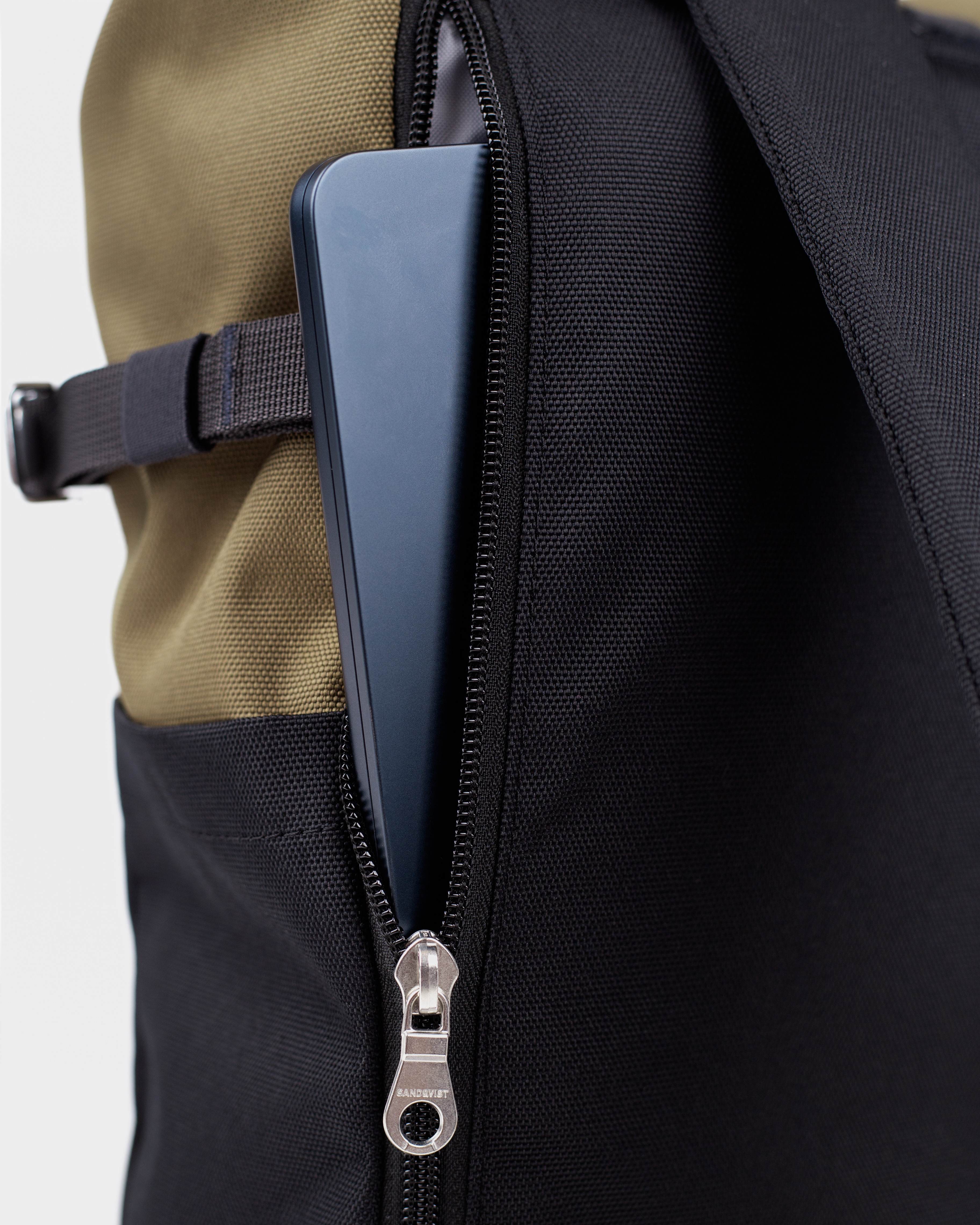 Sandqvist Icon Rolltop Backpack L 16, green and black. Close-up of the outside laptop compartment with a zipper.