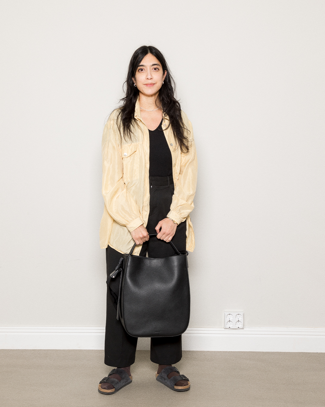 Female model holding the Sandqvist Agile Hobo Tote Bag, black. front view, holding the bag in the handle.