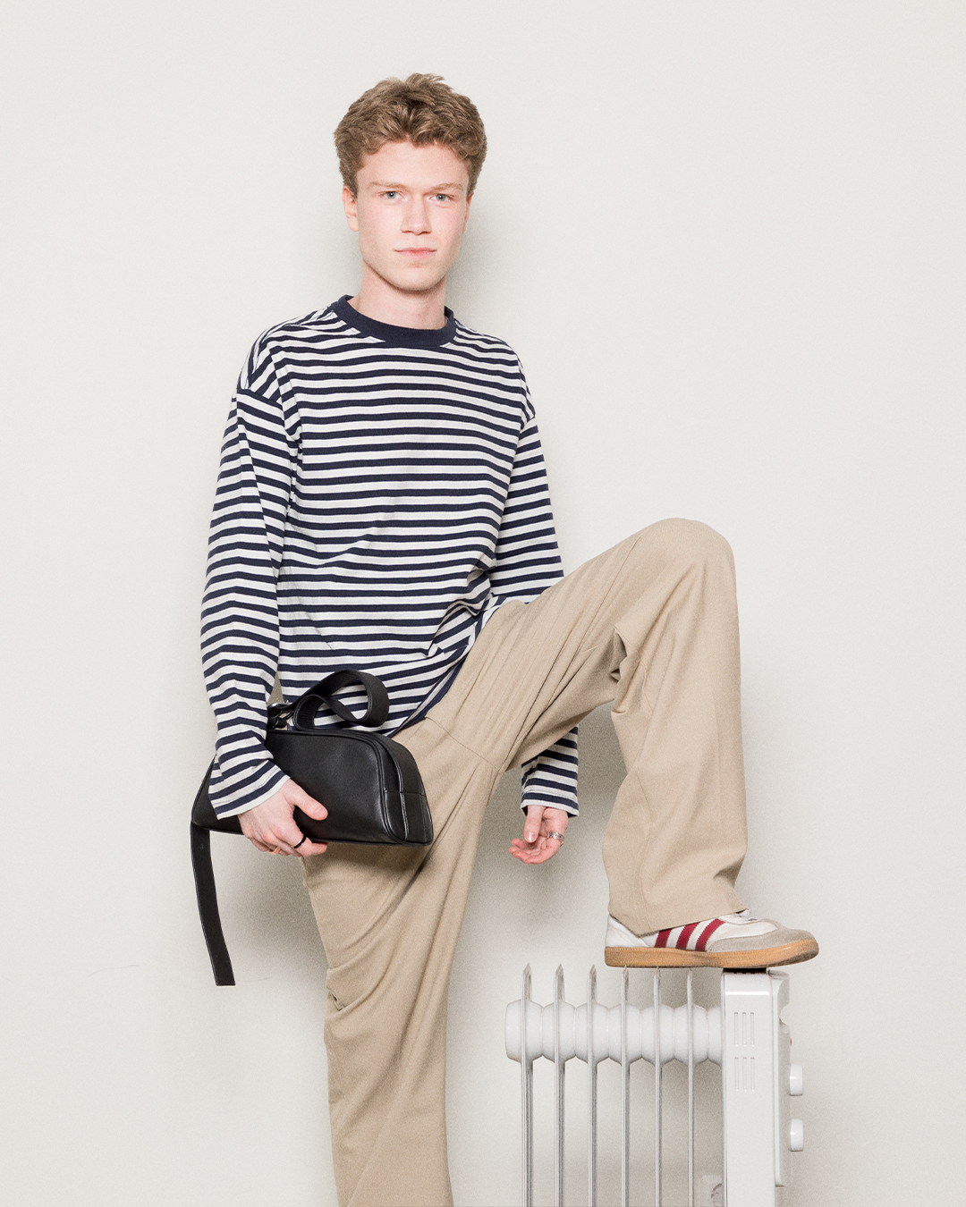 Manlig modell står vid ett element och håller i Sandqvist Leather Baguette Bag.