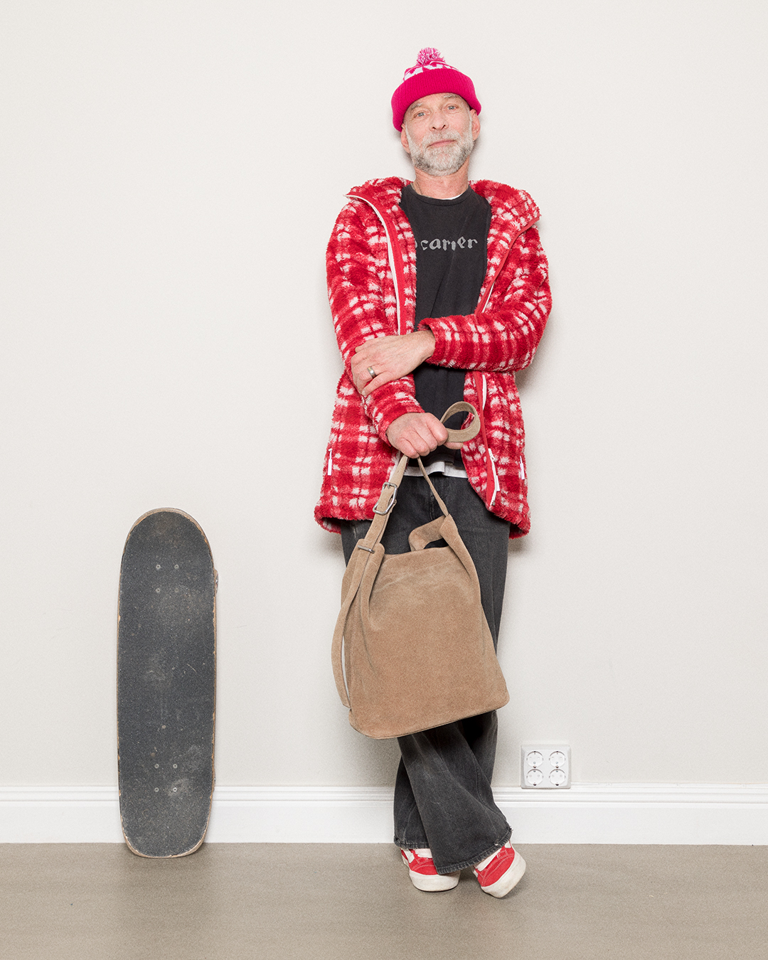 Manlig modell som står bredvid sin skateboard och håller i Sandqvist Leather Suede Shopper Bag, taupe. Framifrån, håller i väskan i handtaget.