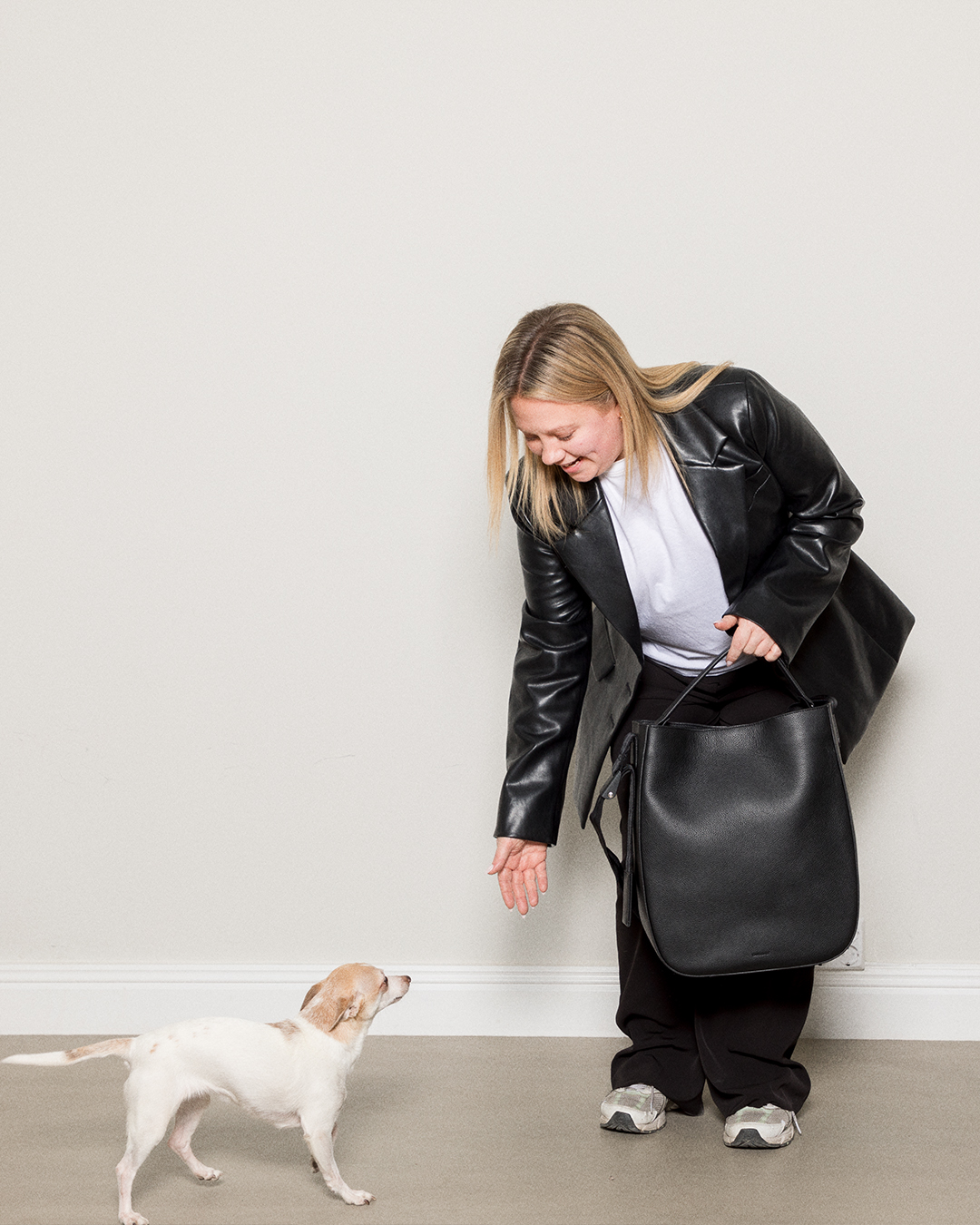 Female model holding the Sandqvist Agile Tote Bag, black. Front view, holding it in the handle, while petting a dog.