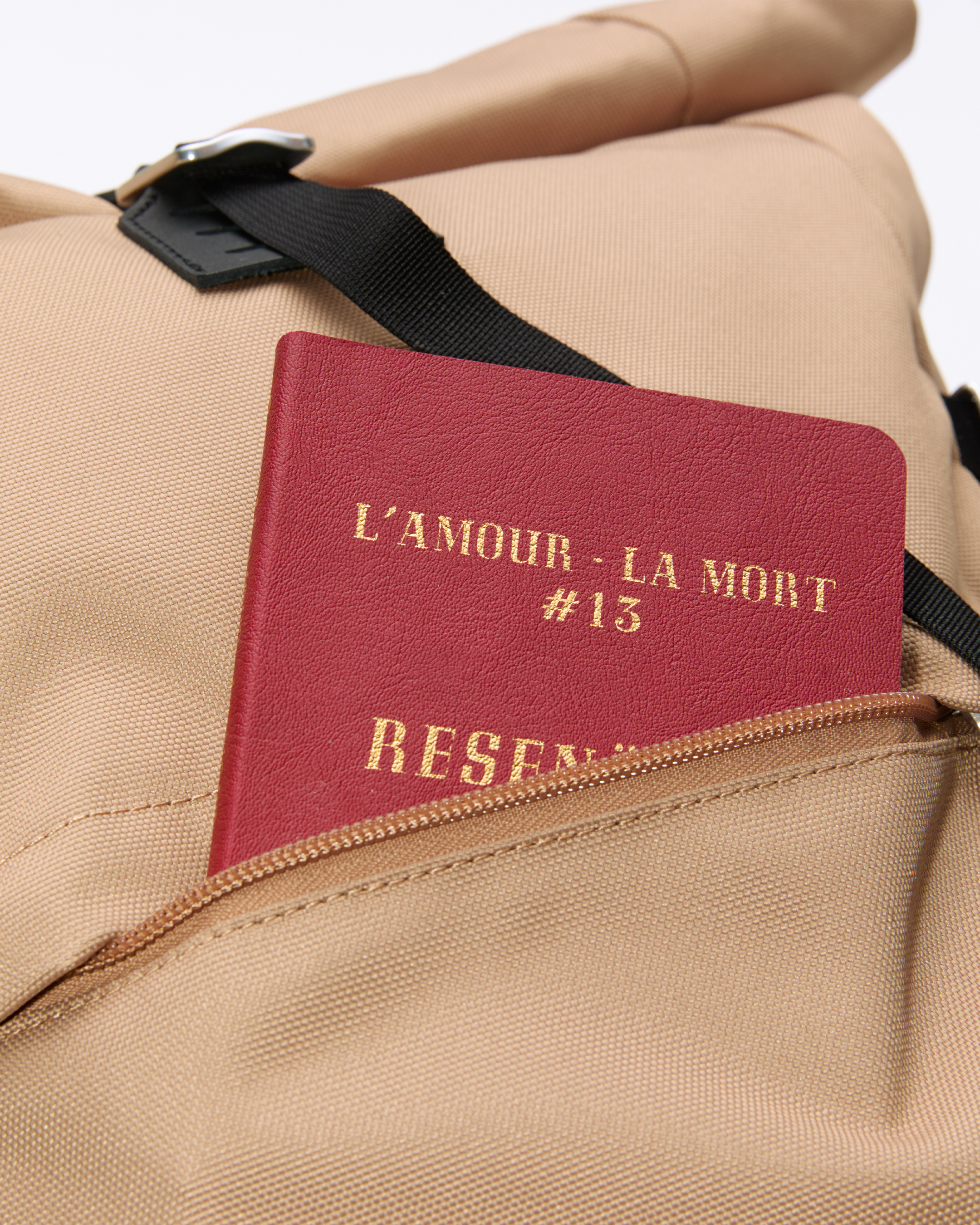 Sandqvist ICON Rolltop Backpack 16”, beige. Close-up of the front pocket with a book sticking out.