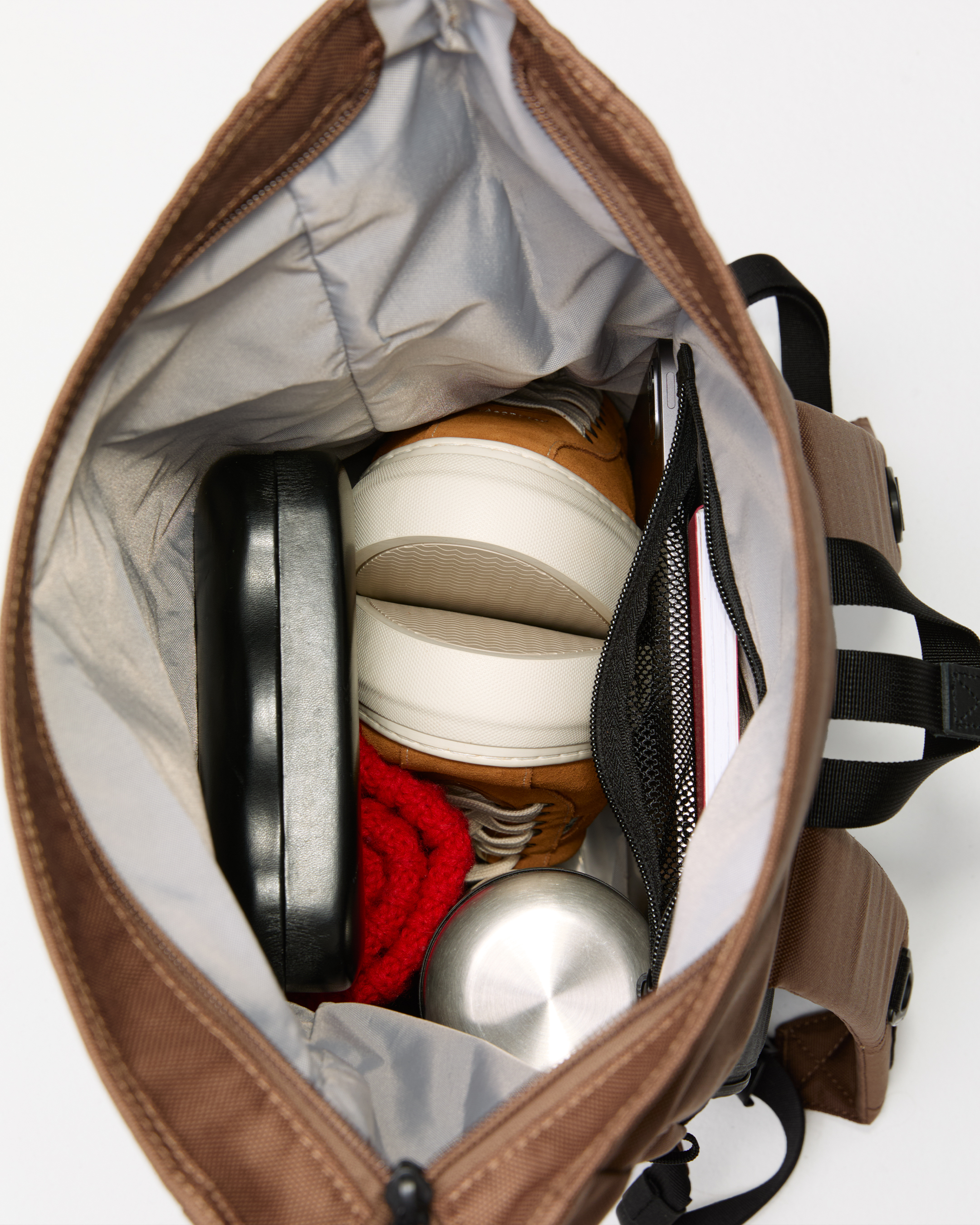 Sandqvist ICON Rolltop Backpack 14”, beige. Top view, showing the bags main compartment with opened zippered packed with a book, a pair of shoes, a hat, a food container and a spectacle case.