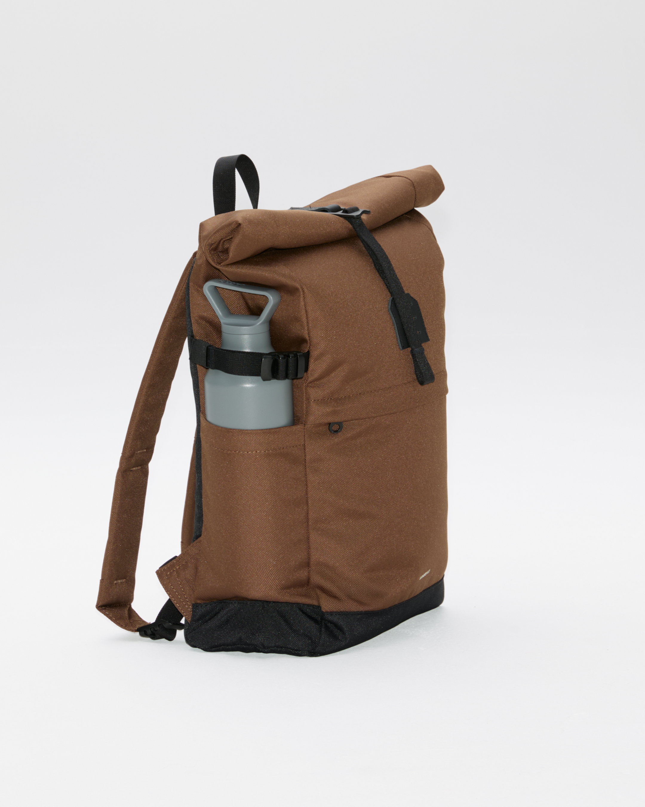 Sandqvist ICON Rolltop Backpack 14”, brown. Side view showing the side slip pocket packed with a waterbottle secured with the side strap.