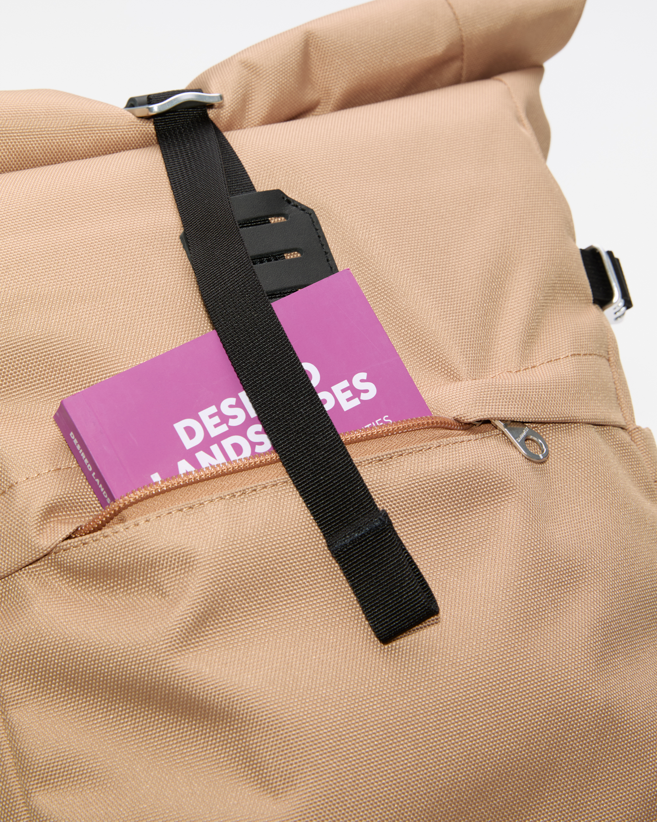 Sandqvist ICON Rolltop Backpack 14”, beige. Close-up of the front pocket with a book sticking out.