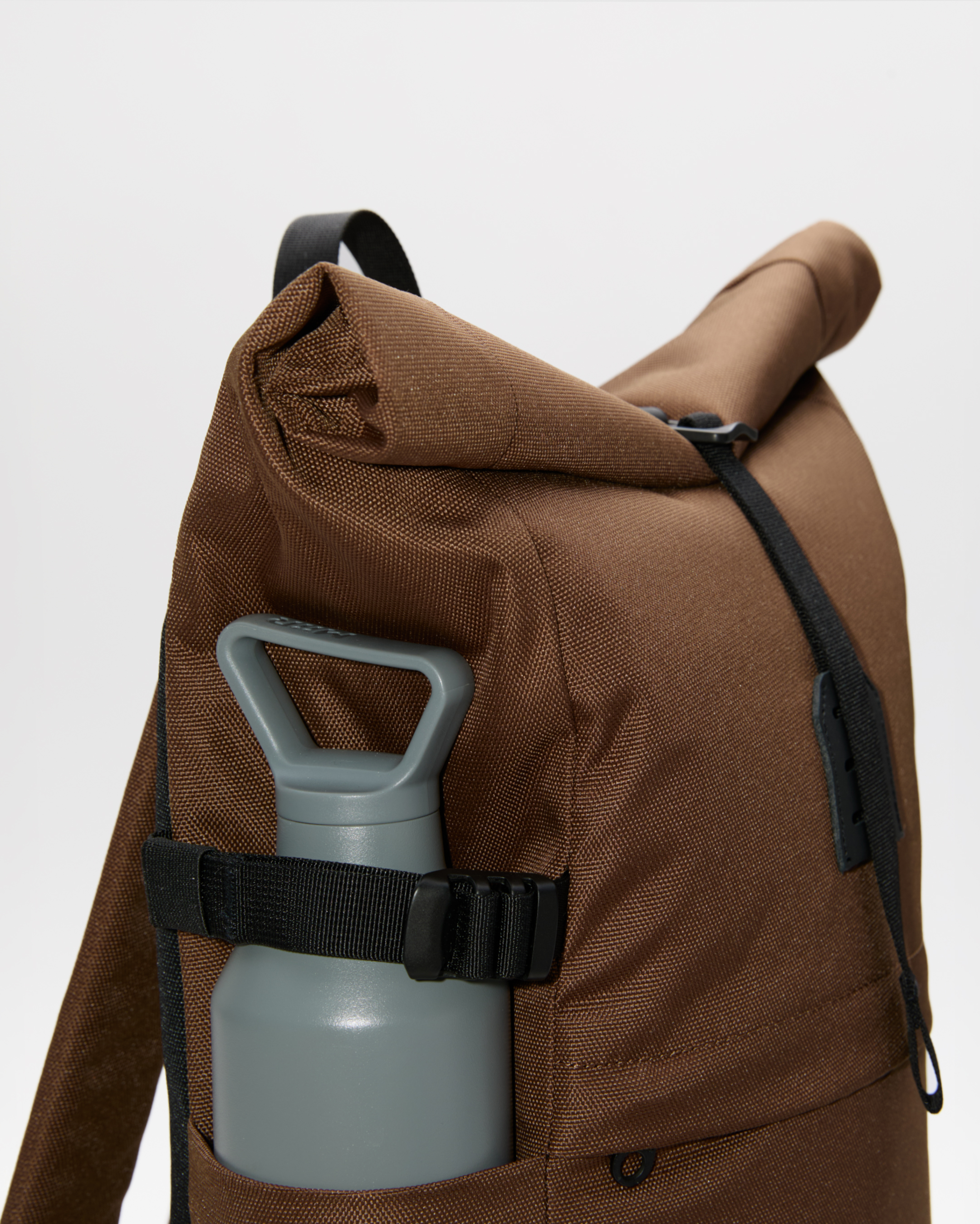 Backpack, Sandqvist ICON Rolltop Backpack 14”, brown. Close up side view showing the side slip pocket packed with a waterbottle secured with the side strap.
