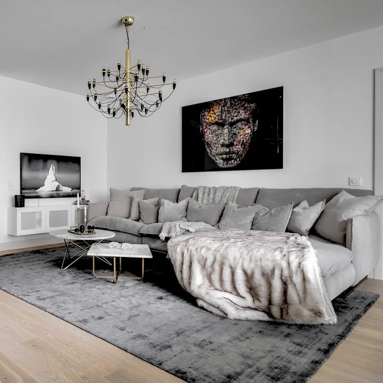 Lysegrå divansofa i 100% polyesterfløyel med komfortable sitte- og ryggputer fylt med dun. Pelspledd i hvitt, imitert pels, 150x200 cm.