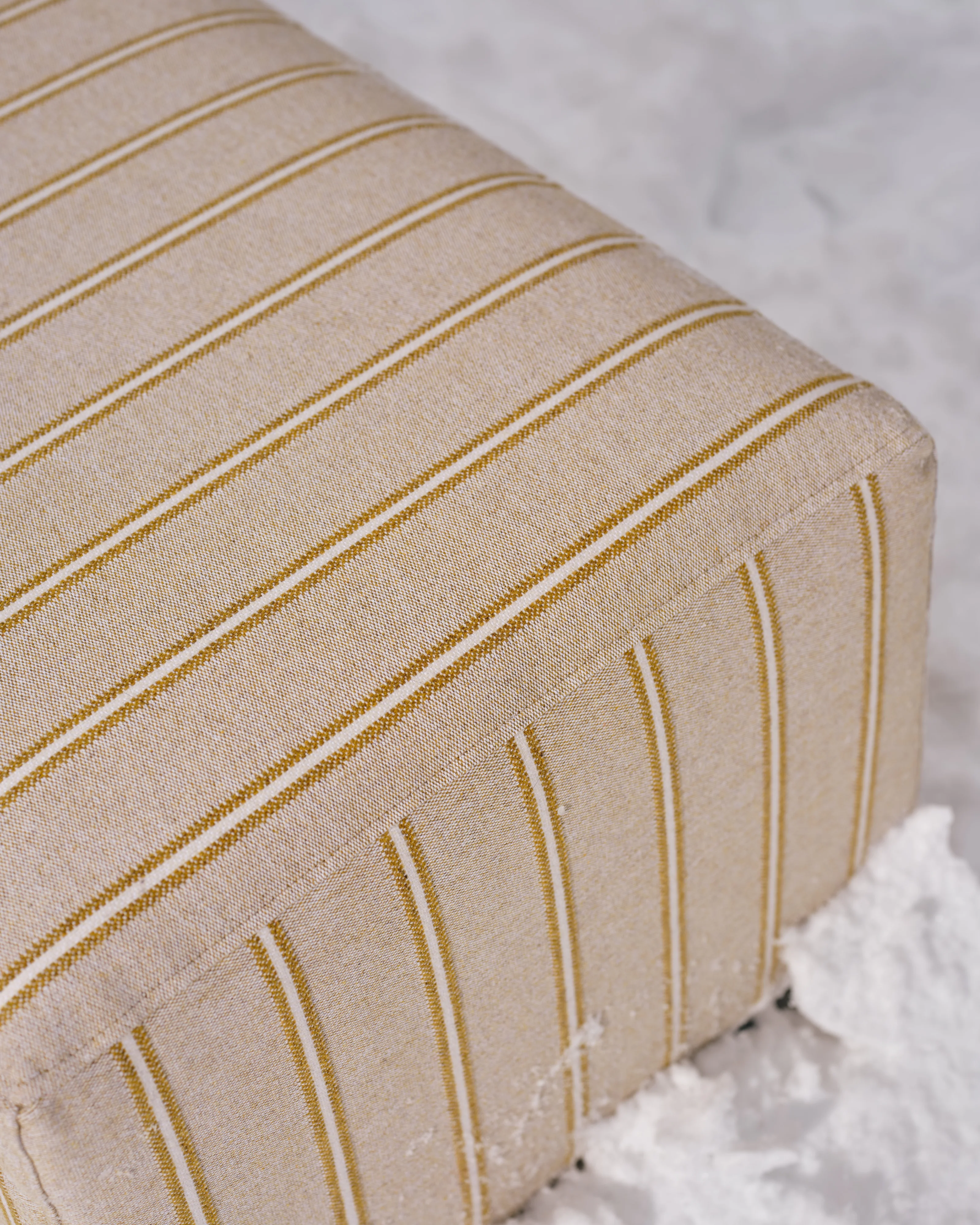 Nærbilde av et hjørne av Hajen-fotskammel i stripet beige/hvitt stoff, stående i snøen.